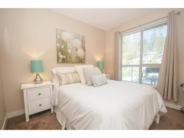 Bright bedroom with white bedding, teal accents, and a large window with blinds. - 418 - 1633 Mackay Avenue, North Vancouver