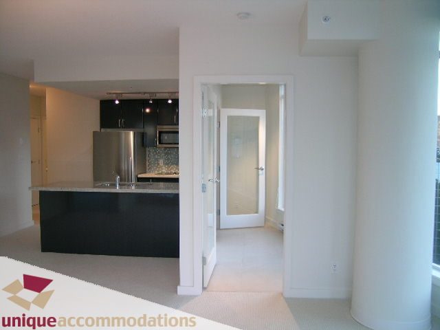 Bright kitchen with black countertops and stainless steel appliances, leading to a cozy den area. - 1101 - 1188 West Pender, Vancouver Downtown