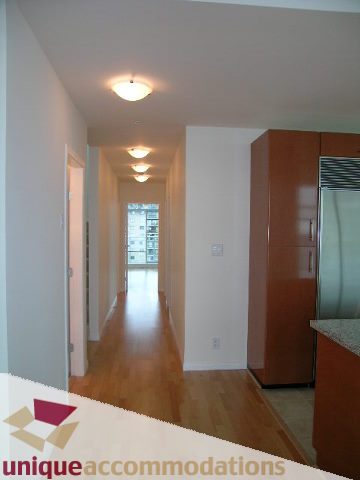 Bright kitchen with wooden cabinets and hardwood floors, leading to a spacious living area. - 2301 - 188 E Esplanade, North Vancouver