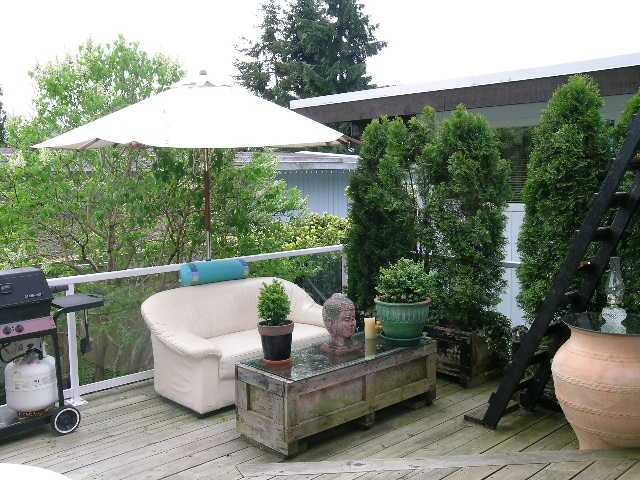 Furnished living room with a glass coffee table, outdoor patio, and trees in the background. - 470 Ellis Street, North Vancouver