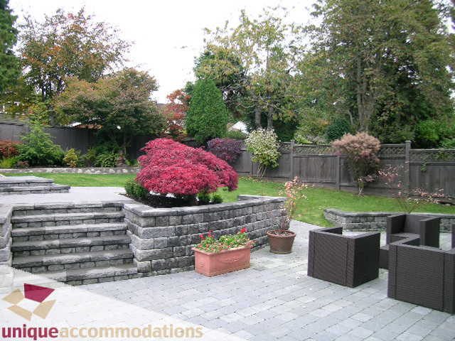 Furnished patio with stone seating and potted plants, surrounded by greenery. - 1365 Kings Ave, West Vancouver
