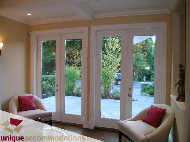 Bright living room with French doors opening to garden, hardwood floors, and cozy armchairs. - 1365 Kings Ave, West Vancouver