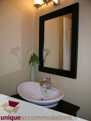 Bathroom with black countertop and white sink, modern mirror reflecting calla lilies. - 1365 Kings Ave, West Vancouver