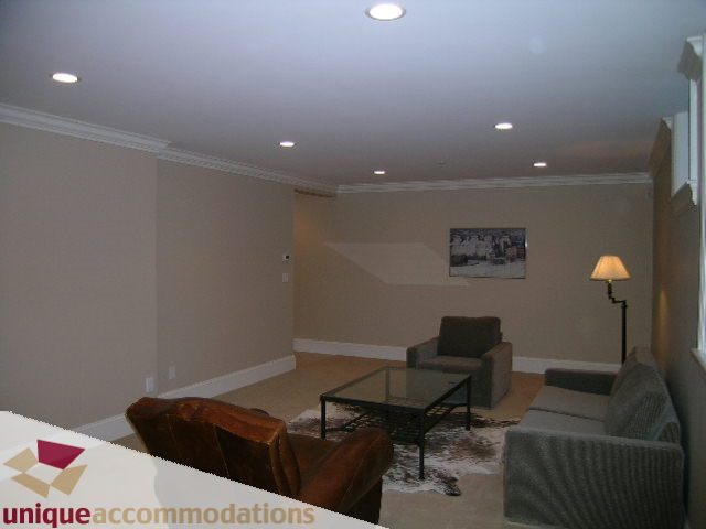 Furnished living room with beige walls, modern lighting, and a cozy sofa setup. - 1365 Kings Ave, West Vancouver
