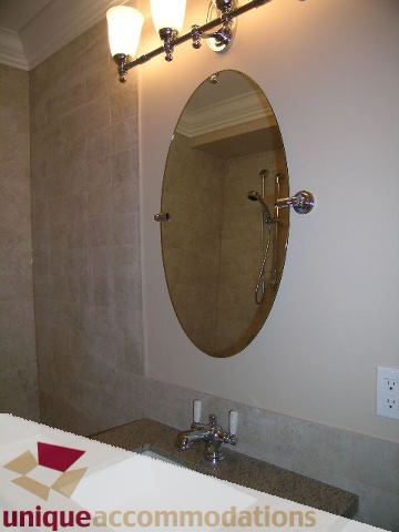 Bathroom with large oval mirror, modern fixtures, and beige stone walls. - 1365 Kings Ave, West Vancouver