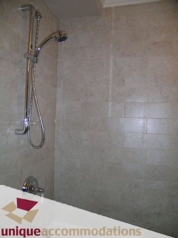 Bathroom with modern shower setup and beige tile walls. - 1365 Kings Ave, West Vancouver
