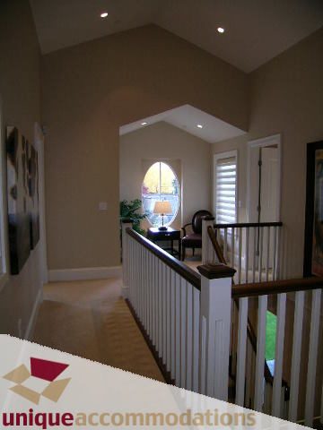 Staircase leading to upper level with white railings and natural light from arched window. - 1365 Kings Ave, West Vancouver