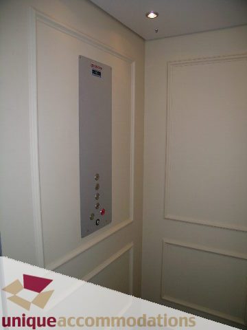 Narrow hallway with white paneling and a control panel on the wall. - 1365 Kings Ave, West Vancouver