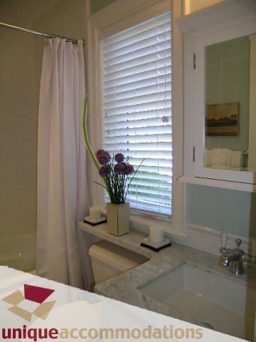 Bathroom with white blinds, marble countertop, and vase of flowers. - 1365 Kings Ave, West Vancouver