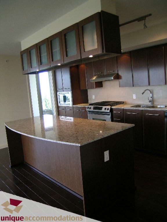 Bright kitchen with granite countertops, dark wood cabinets, and a city view through the window. - 905 - 683 Victoria Park West, North Vancouver