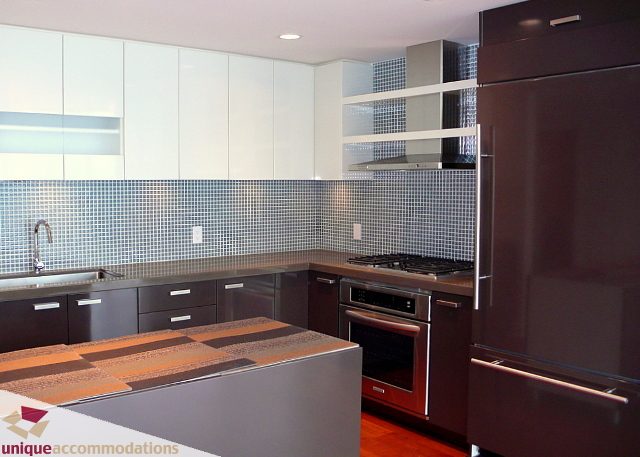 Modern kitchen with sleek black cabinets, granite countertops, and a tile backsplash. - 2802 - 1277 Melville Street, Vancouver Downtown