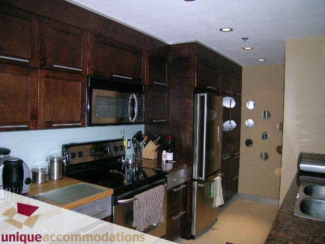 Bright kitchen with dark wood cabinets, granite countertops, and stainless steel appliances. - 2803 - 930 Cambie Street, Vancouver Downtown