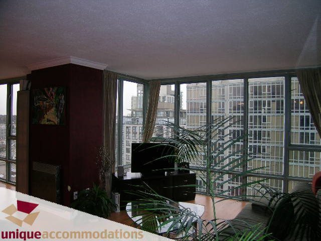 Bright living room with city view and large windows, featuring dark wood furniture and greenery. - 2803 - 930 Cambie Street, Vancouver Downtown