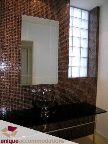 Bathroom with mosaic tile walls, black countertop, and large mirror. - 104 - 1139 West Cordova Street, Vancouver Downtown