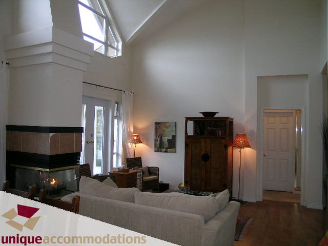 Spacious living room with vaulted ceiling, large windows, and a cozy fireplace. - 604 - 3600 Windcrest Drive, North Vancouver