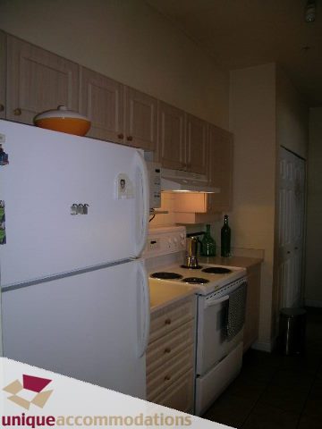 Bright kitchen with white appliances, light wood cabinets, and a small window. - 604 - 3600 Windcrest Drive, North Vancouver