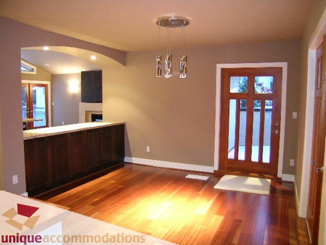 Bright living room with hardwood floors and modern chandelier, leading to a kitchen with dark cabinetry. - 811 Huntingdon Crescent, North Vancouver
