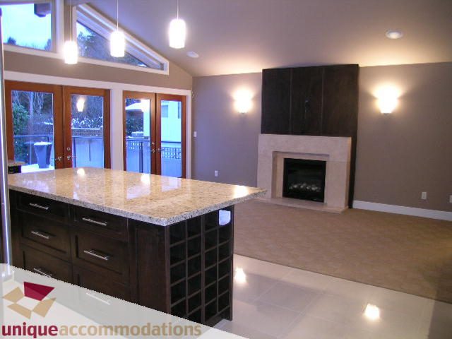 Bright kitchen with granite countertops and a wine rack, leading to a cozy living area with a fireplace and large windows.
