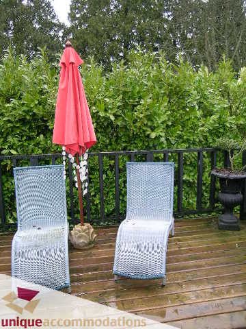 Furnished patio with wicker chairs and red umbrella, surrounded by greenery. - 840 16th Street, West Vancouver