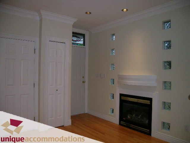 Living room with hardwood floors and a fireplace, featuring decorative glass panels on the wall. - 1055 West 15th Avenue, Vancouver West Side