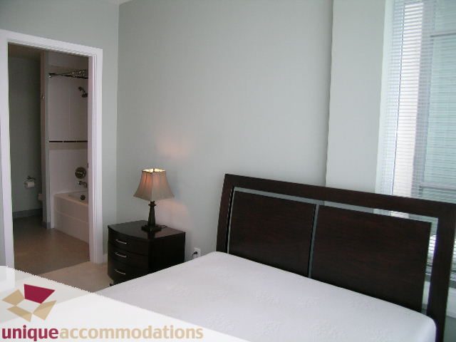 Furnished bedroom with dark wood headboard and nightstand, adjacent bathroom with shower. - 702 - 2055 Yukon Street, Vancouver West Side