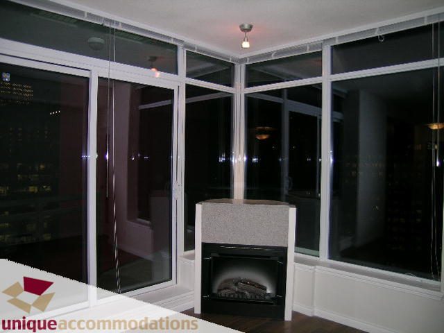 Spacious living room with large windows offering a stunning city view, featuring a modern fireplace and sleek countertops.