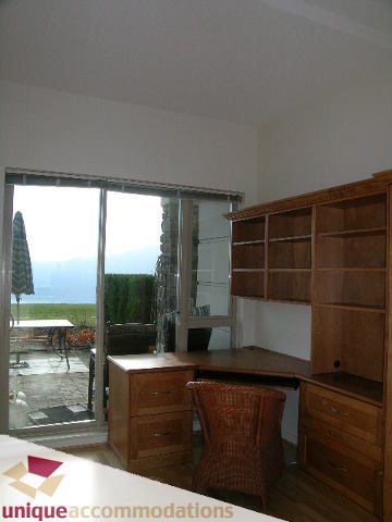 Bright living room with wooden cabinets, city view, and natural light from sliding glass doors. - 109 - 530 Raven Woods seasons south, North Vancouver