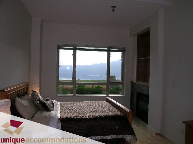 Furnished bedroom with large window view, hardwood floors, and cozy bedding. - 109 - 530 Raven Woods seasons south, North Vancouver