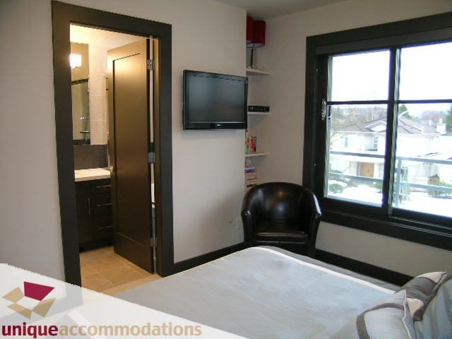 Furnished bedroom with a large window, a flat-screen TV, and a modern bathroom in the background. - 2429 West 19th Avenue, Vancouver West Side
