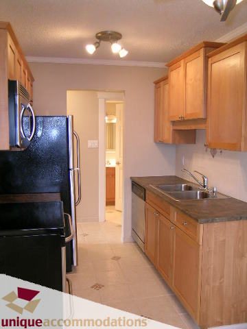 Bright kitchen with black countertops and wooden cabinets, featuring a modern sink and tiled flooring. - 110 - 225 West 3rd Street, North Vancouver