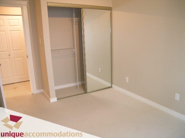Spacious bedroom with mirrored closet doors and beige carpeting. - 110 - 225 West 3rd Street, North Vancouver