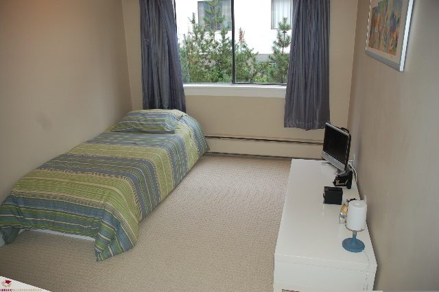 Bright bedroom with striped bedding and city view. - 110 - 225 West 3rd Street, North Vancouver