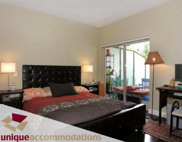 Bright and cozy bedroom with a large bed, wooden nightstands, and a sliding glass door leading to a balcony.