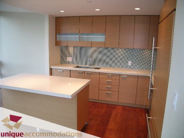 Modern kitchen with light wood cabinets, white countertops, and a mosaic tile backsplash. - 2401-1277 Melville, Vancouver Downtown