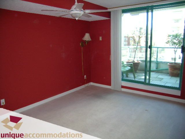 Living room with red walls, carpeted floor, and sliding glass door leading to a patio. - 703 - 1132 Haro Street, Vancouver Downtown