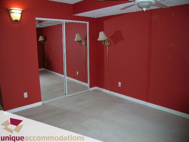 Bright bedroom with red walls, carpeted floor, and wall-mounted lamps. - 703 - 1132 Haro Street, Vancouver Downtown
