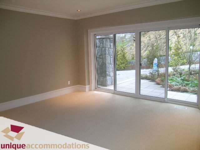 Spacious living room with large windows and stone wall, leading to a patio. - 2550 Marr Creek Ct, West Vancouver