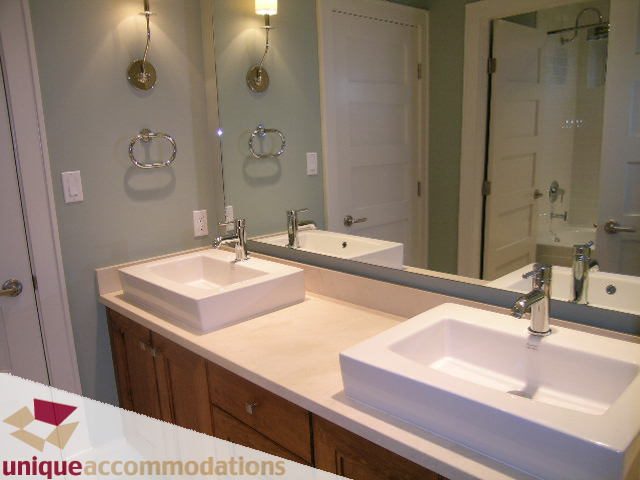Bathroom with white vessel sinks, light wood cabinets, and a large mirror. - 2550 Marr Creek Ct, West Vancouver
