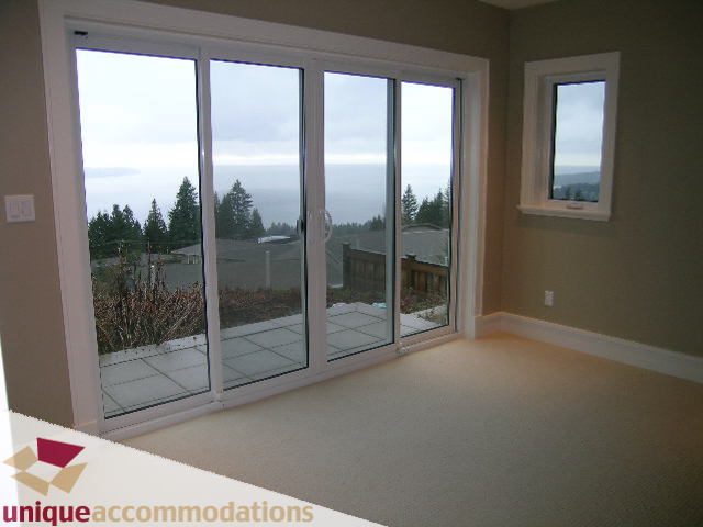 Bright living room with sliding glass doors, ocean view, and carpeted floors. - 2550 Marr Creek Ct, West Vancouver