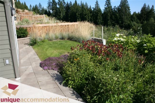 Furnished patio with lush greenery and wildflowers, surrounded by trees. - 2550 Marr Creek Ct, West Vancouver