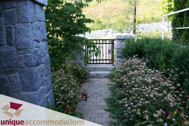 Furnished patio with stone wall, brick path, and blooming flowers. - 2550 Marr Creek Ct, West Vancouver
