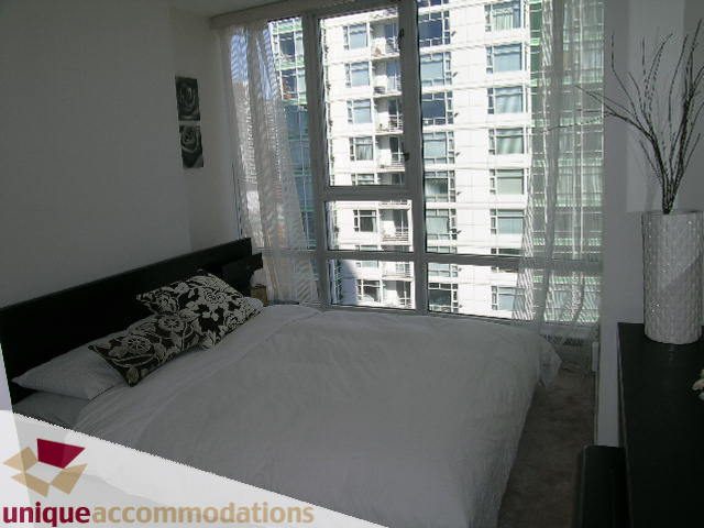 Bright bedroom with large windows and city view, modern decor, and cozy bedding. - 2003 - 1201 Marinaside Crescent, Vancouver Downtown