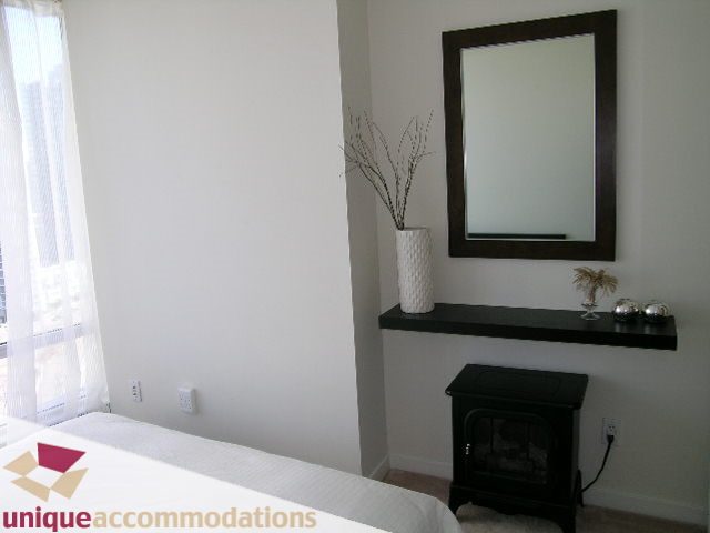 Bright bedroom with dark wood stove, white walls, and sheer curtains. - 2003 - 1201 Marinaside Crescent, Vancouver Downtown