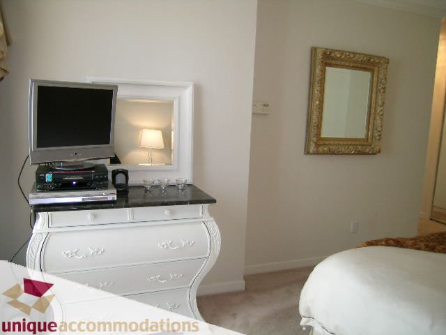 Bright bedroom with white dresser, gold-framed mirror, and flat-screen TV on countertop. - 2003 - 1201 Marinaside Crescent, Vancouver Downtown