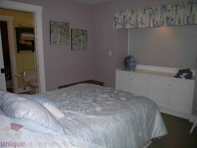 Furnished bedroom with white cabinets, floral bedding, and a window with blinds. - 4221 Rockridge Crescent, West Vancouver