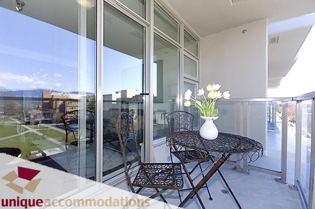 Furnished balcony with glass railings, city view, and white tulips in vase. - 505 - 1808 West 1st Avenue, Vancouver West Side