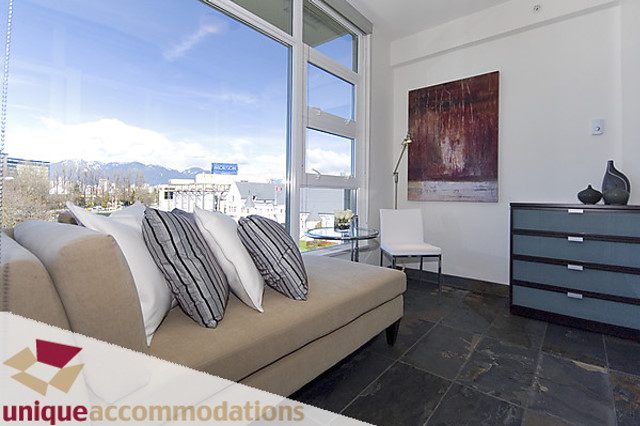 Bright living room with city view and modern decor, featuring a large abstract painting and a sleek coffee table.