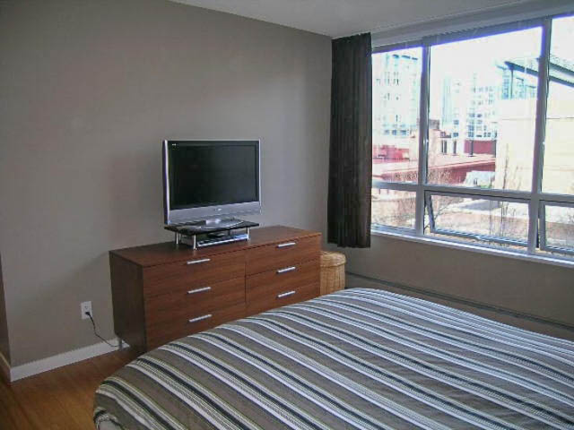 Spacious bedroom with large windows offering city views, neatly made bed, and modern TV setup. - 5D - 139 Drake Street, Vancouver Downtown
