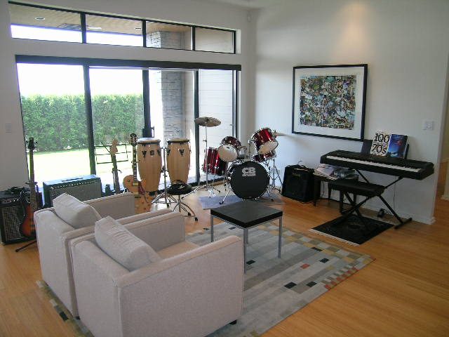 Bright living room with hardwood floors, large windows, and a drum set. - 2456 Hudson Court, West Vancouver