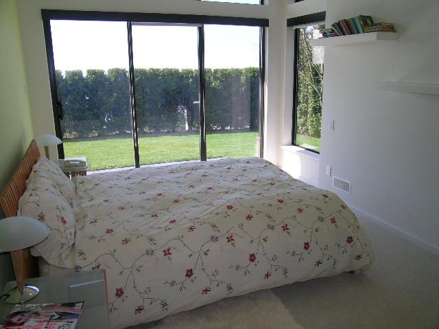 Bright bedroom with large windows, floral bedding, and a view of greenery outside. - 2456 Hudson Court, West Vancouver